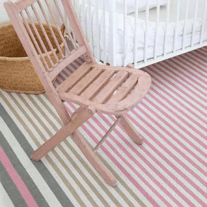 Woven Bliss – Pink chair in front of babies crib on a striped pink and green rug